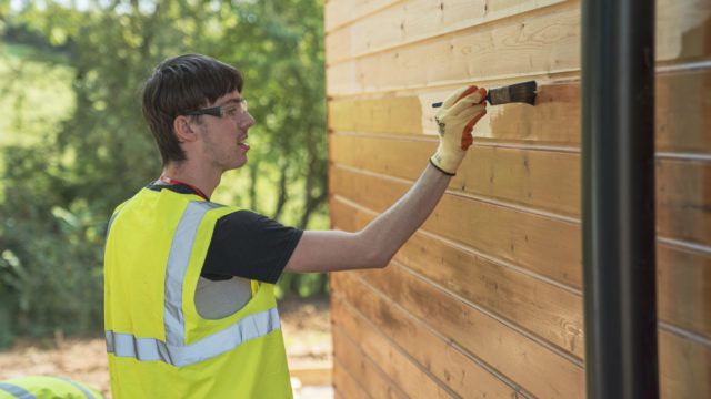 Student painting wooden building at WHM Connections
