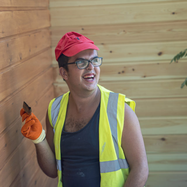 Student smiling whilst painting wooden building