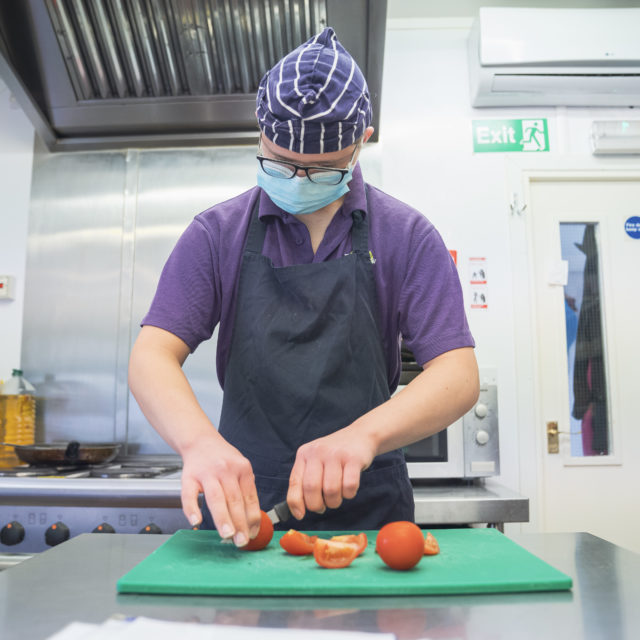 Student chopping tomatoes in commercial kitchen